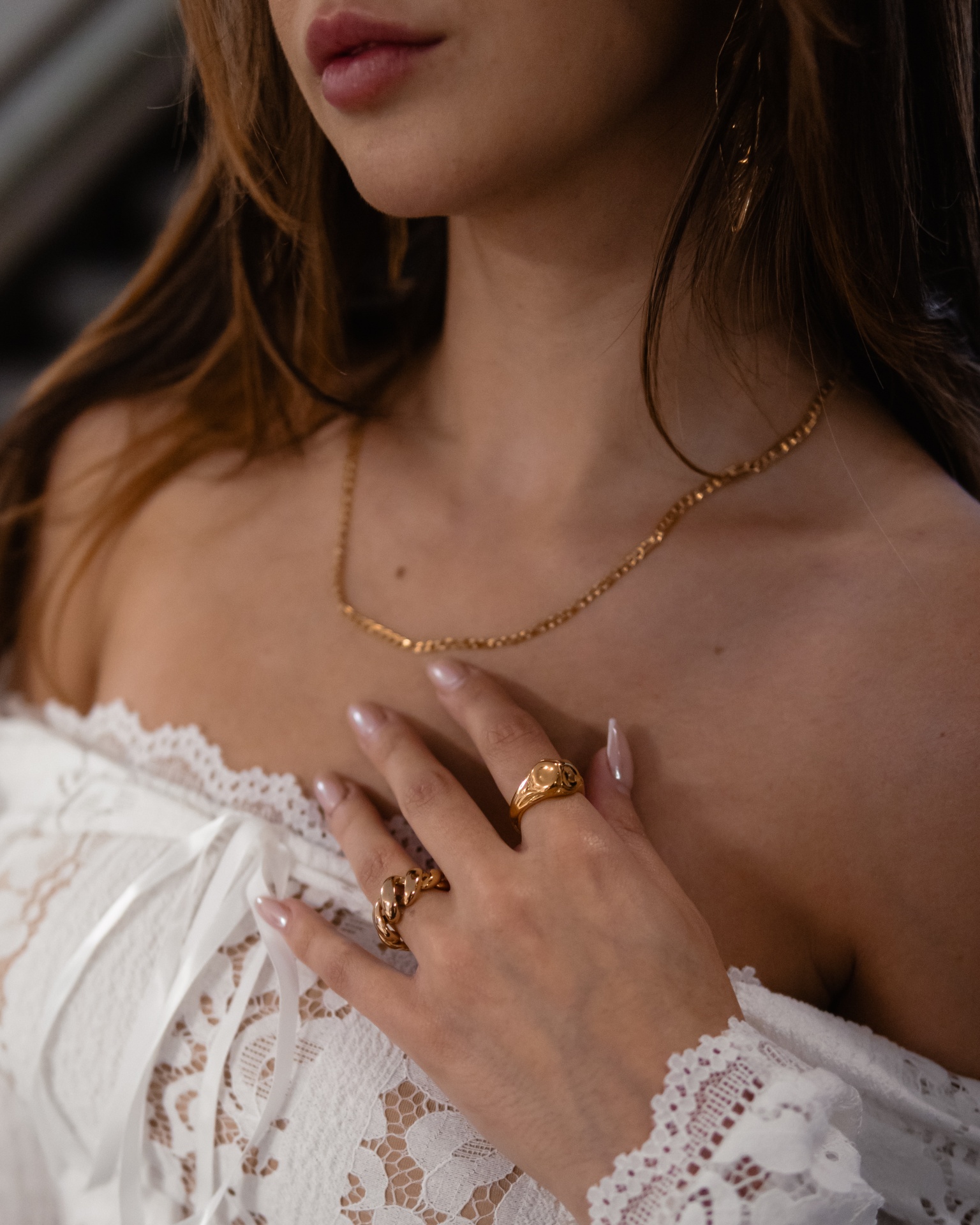 Mulher com colar dourado, anéis dourados e blusa branca de renda