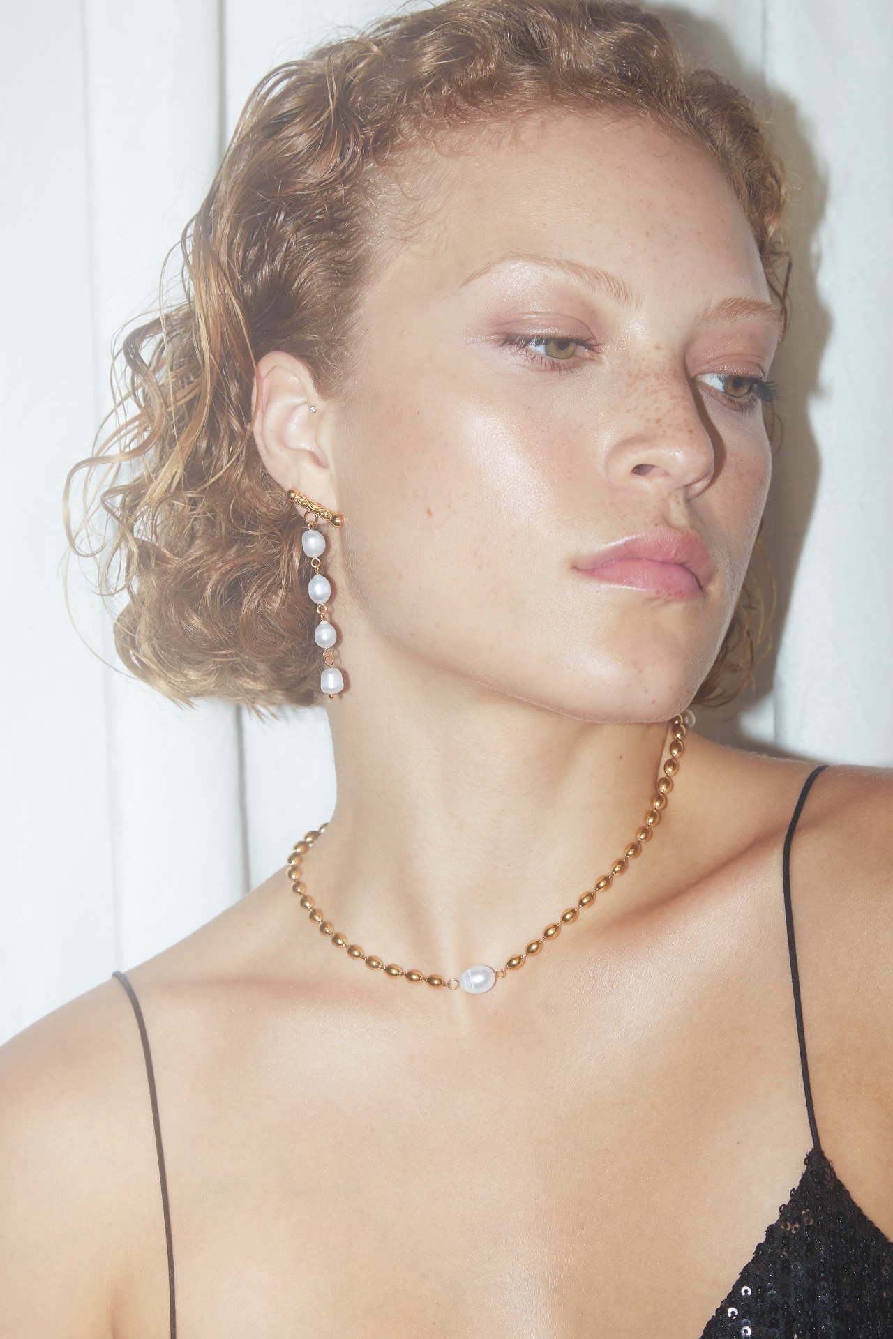 Colar e brinco de pérolas em dourado usados por mulher com top preto.