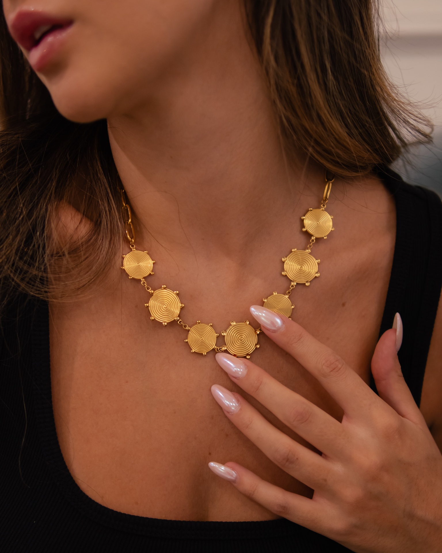 Colar dourado com elementos hexagonais texturizados no pescoço de uma mulher