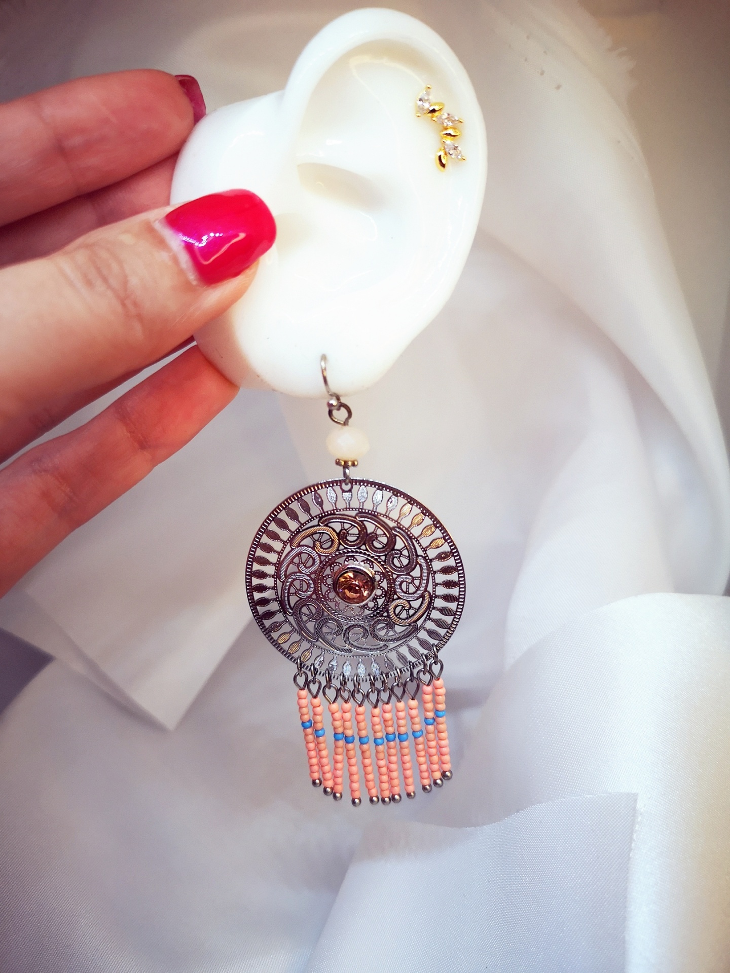 Brinco pendente com contas cor de rosa e azul e detalhe em metal circular em fundo branco