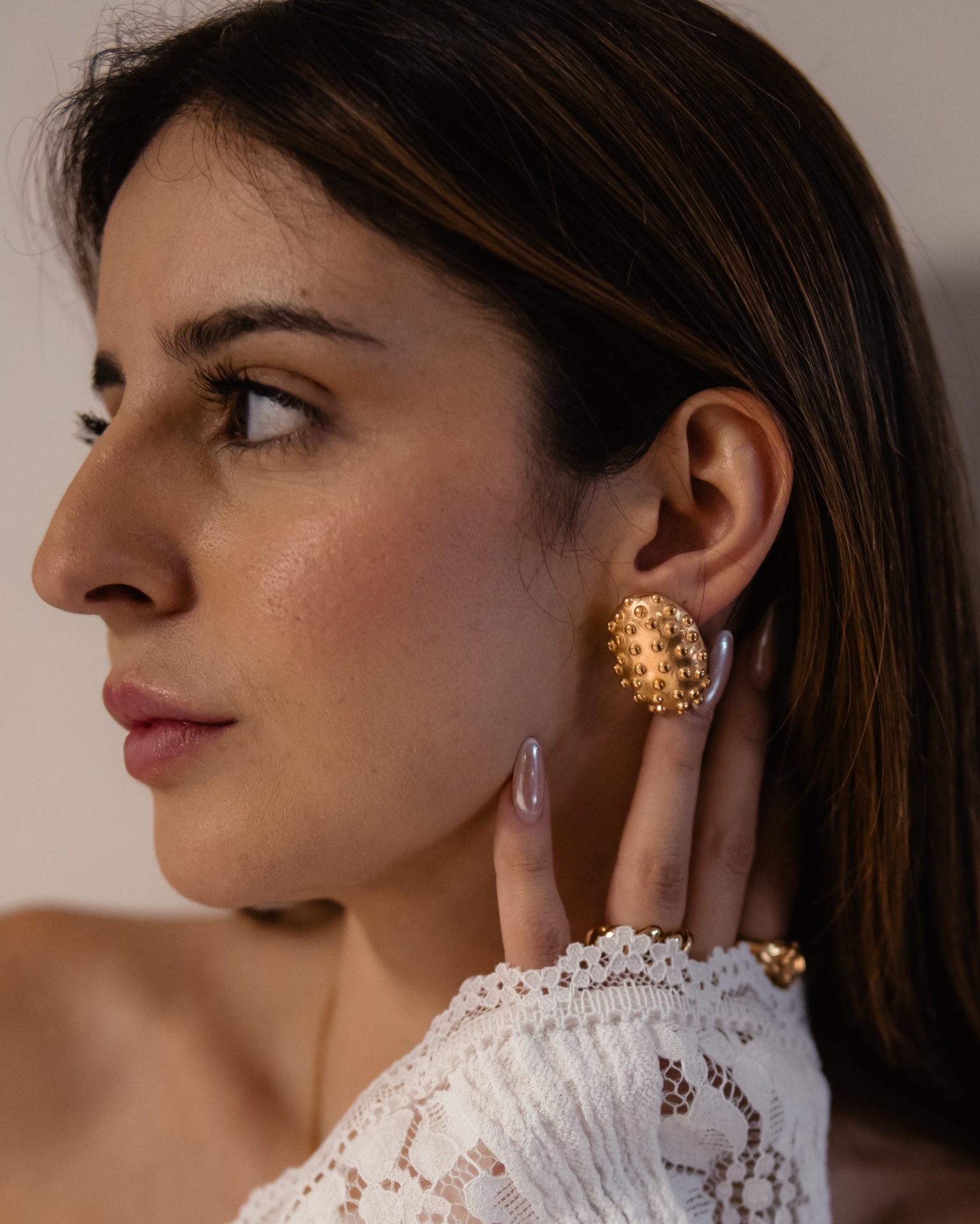 Brincos dourados texturizados em mulher com blusa branca de renda