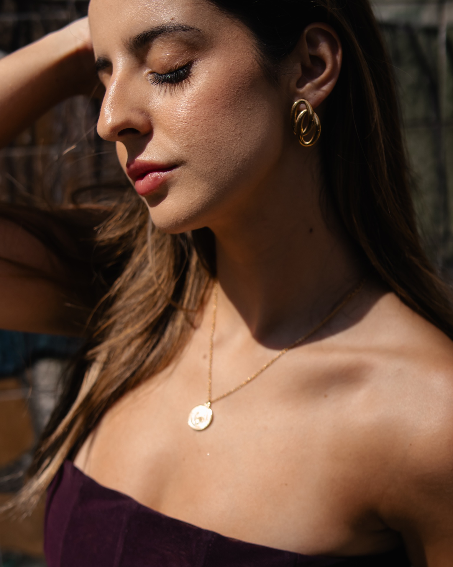 Colar dourado com pendente redondo e brincos dourados usados por mulher.