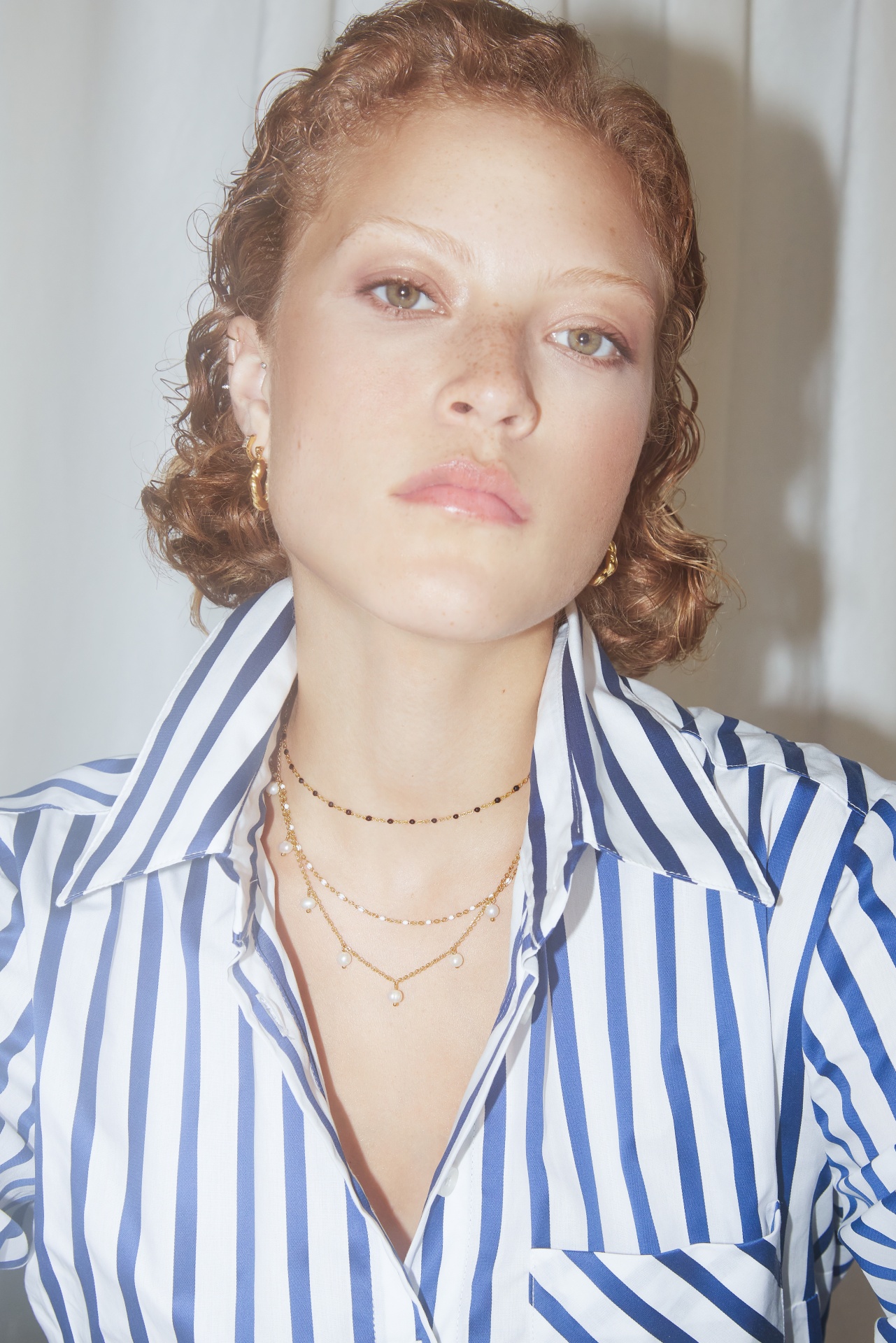 Mulher com camisa listrada azul e branca e colares dourados