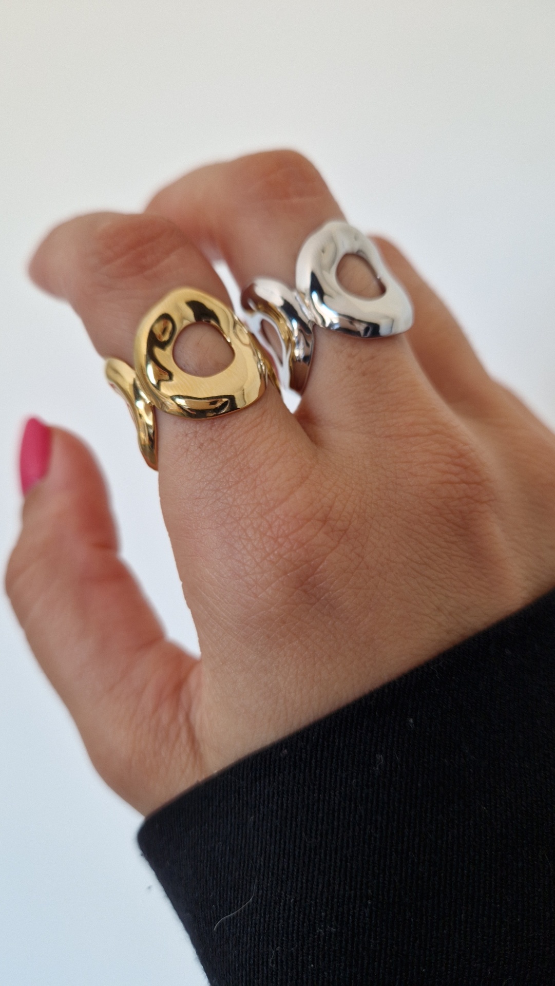 Anéis metálicos dourado e prata com recorte oval em mão com unhas vermelhas