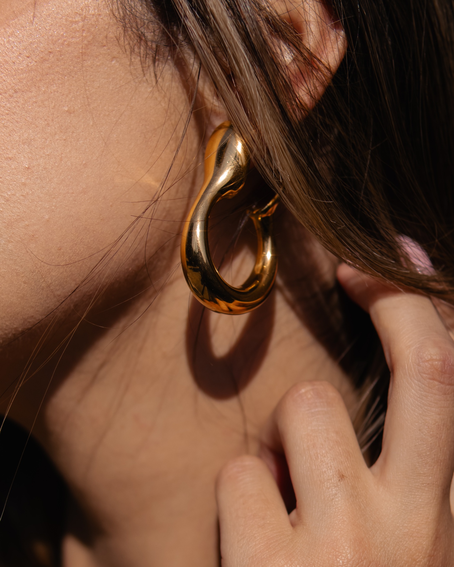 Brinco dourado em design curvo usado na orelha