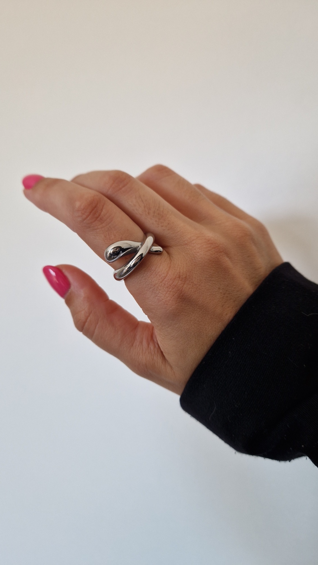 Anel prateado cruzado na mão com unhas rosa