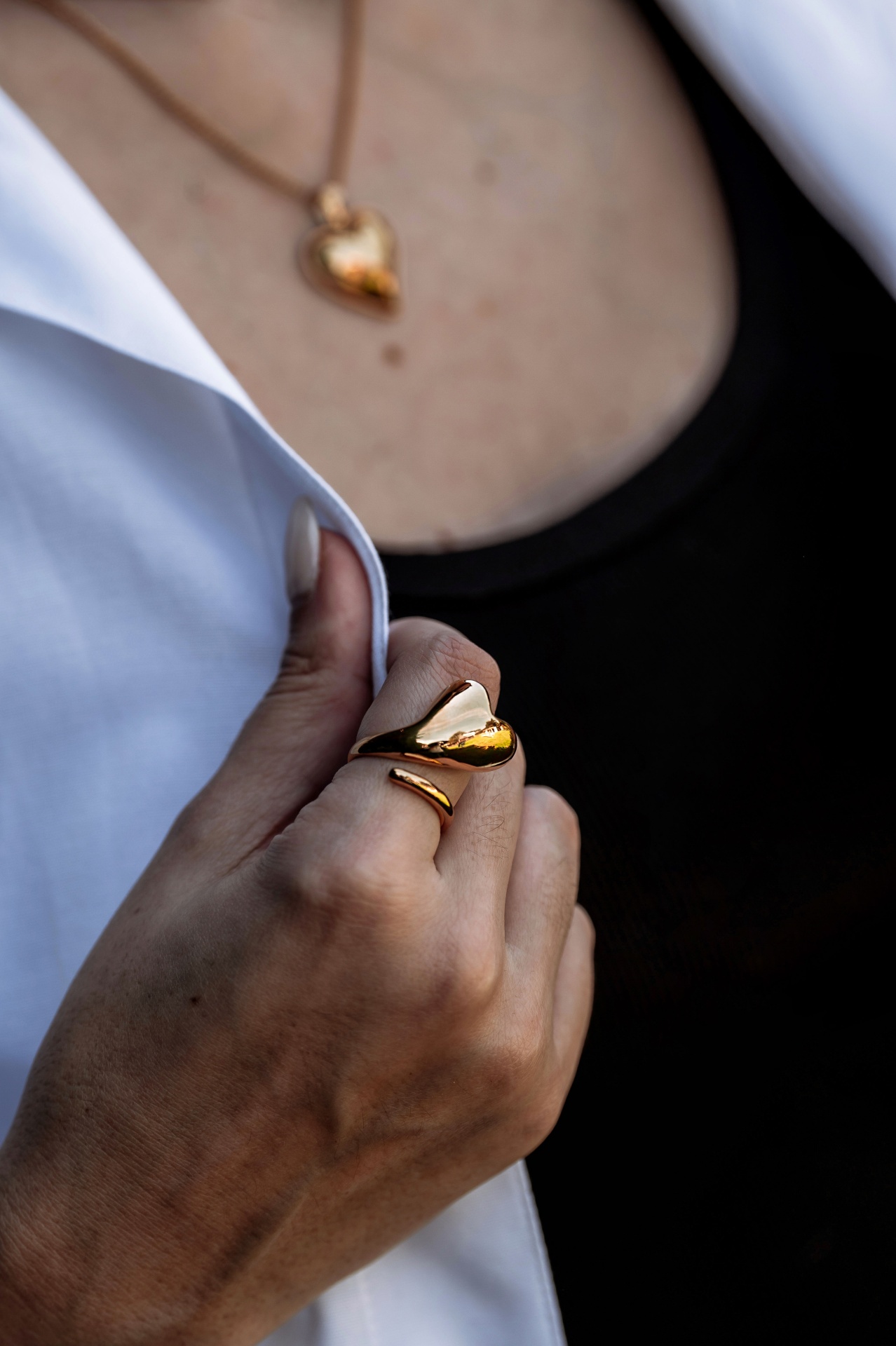 Colar e anel dourados em forma de coração numa pessoa com roupa preta e casaco branco