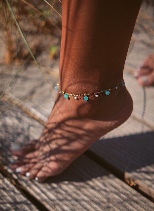 Tornozeleira dourada com contas azuis e pérolas num pé bronzeado