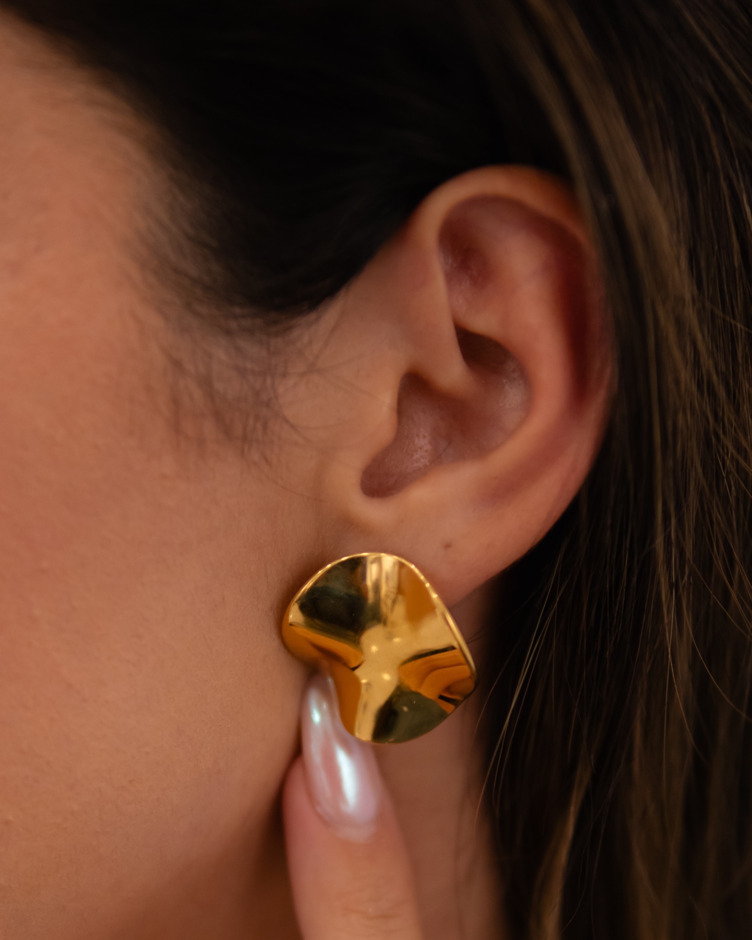 Brinco dourado assimétrico com superfície polida na orelha esquerda.