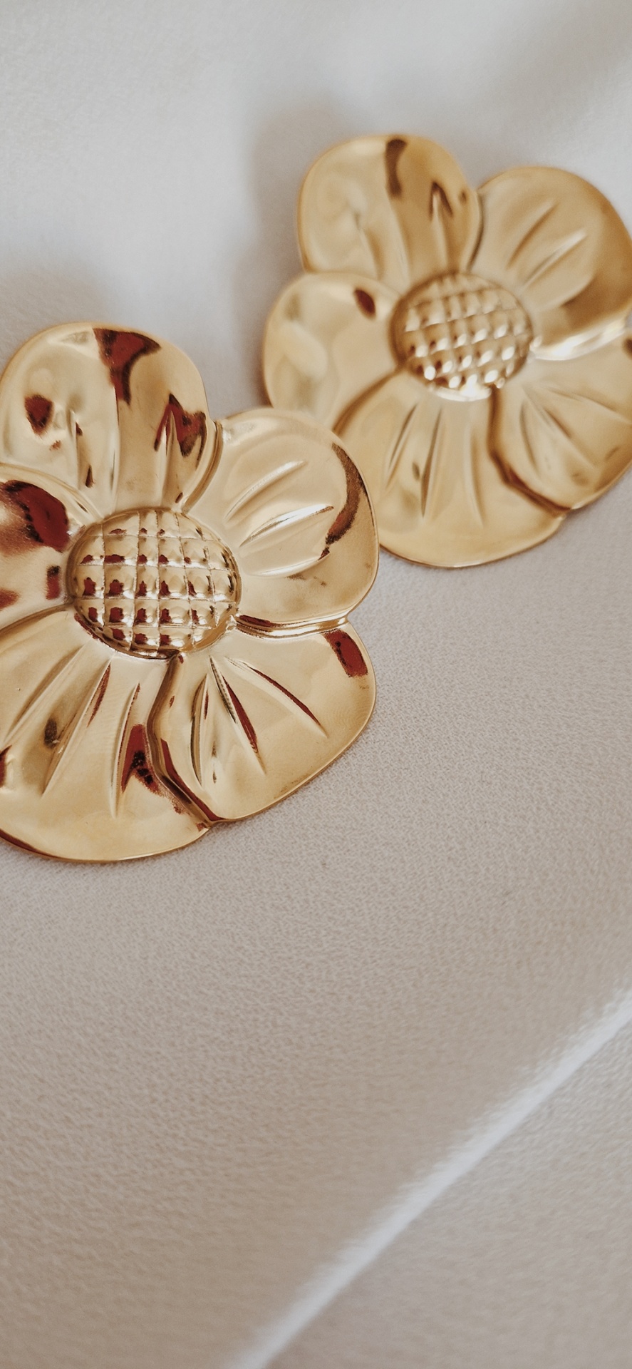 Brincos dourados em forma de flor sobre tecido bege claro