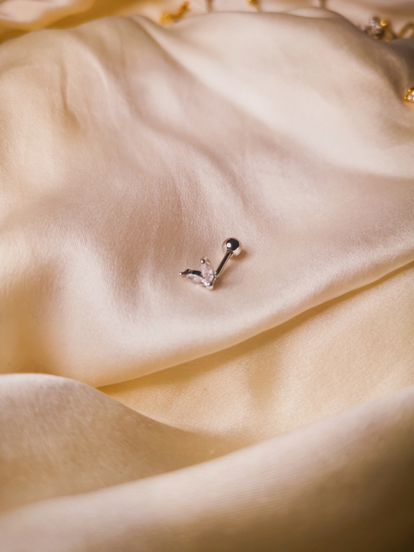 Piercing prateado com pedra transparente sobre tecido branco acetinado