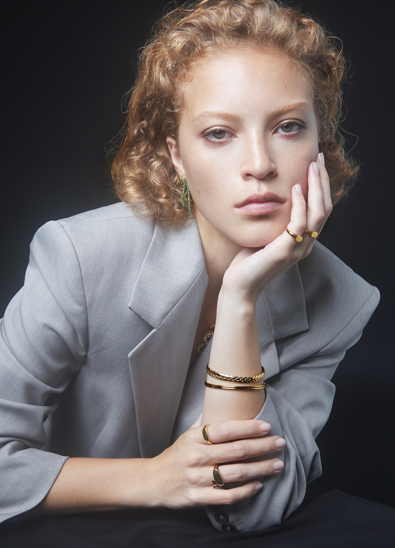 Mulher com casaco cinzento claro e joias douradas e verdes