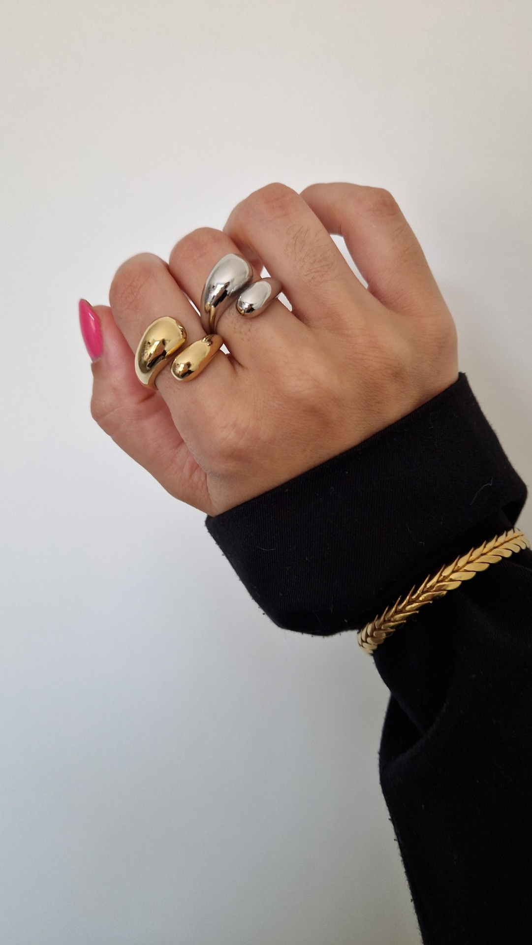 Mão feminina com anéis dourado e prateado, unhas cor-de-rosa e pulseira dourada.