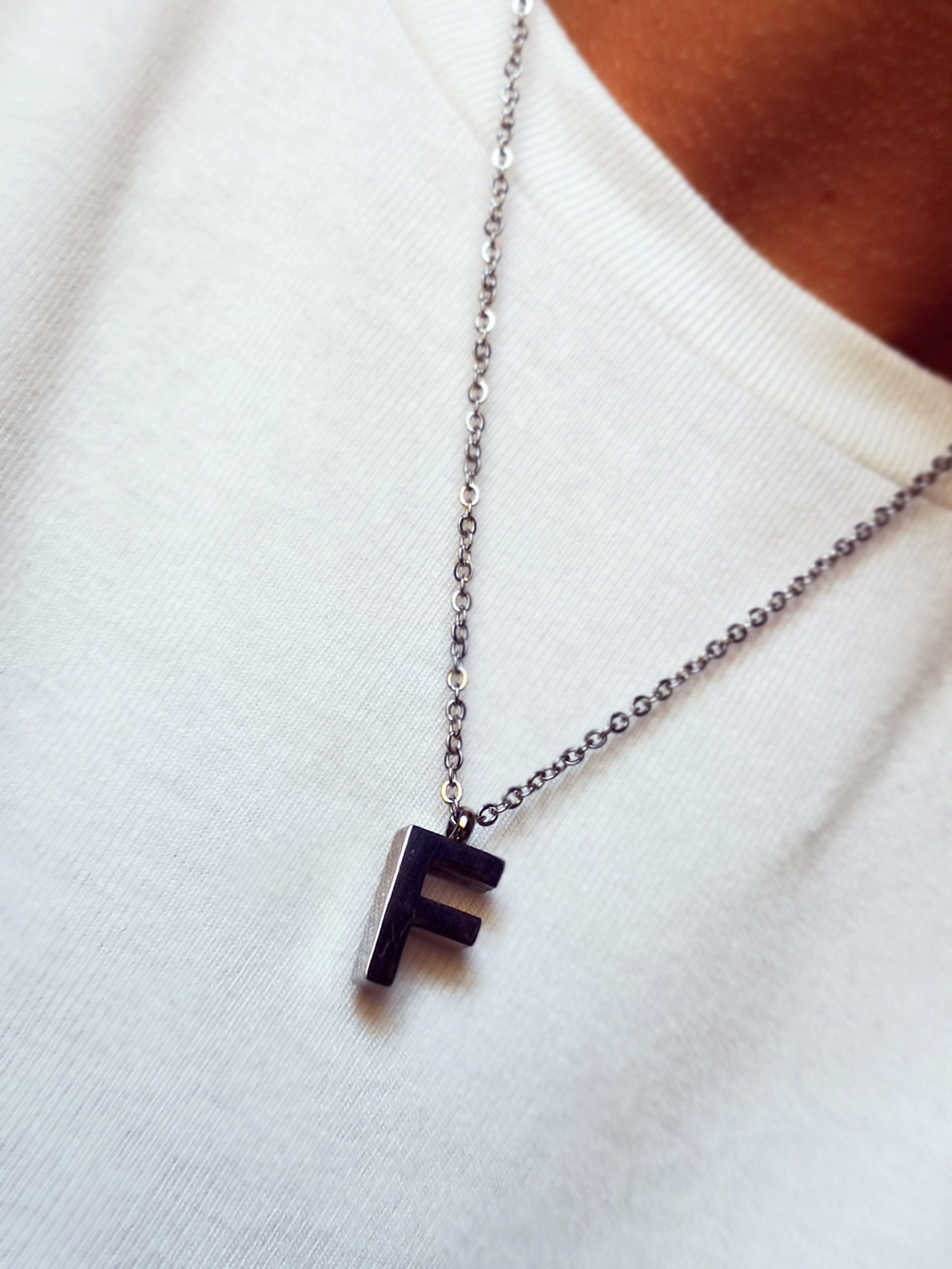 Colar com pingente da letra F preto numa t-shirt branca