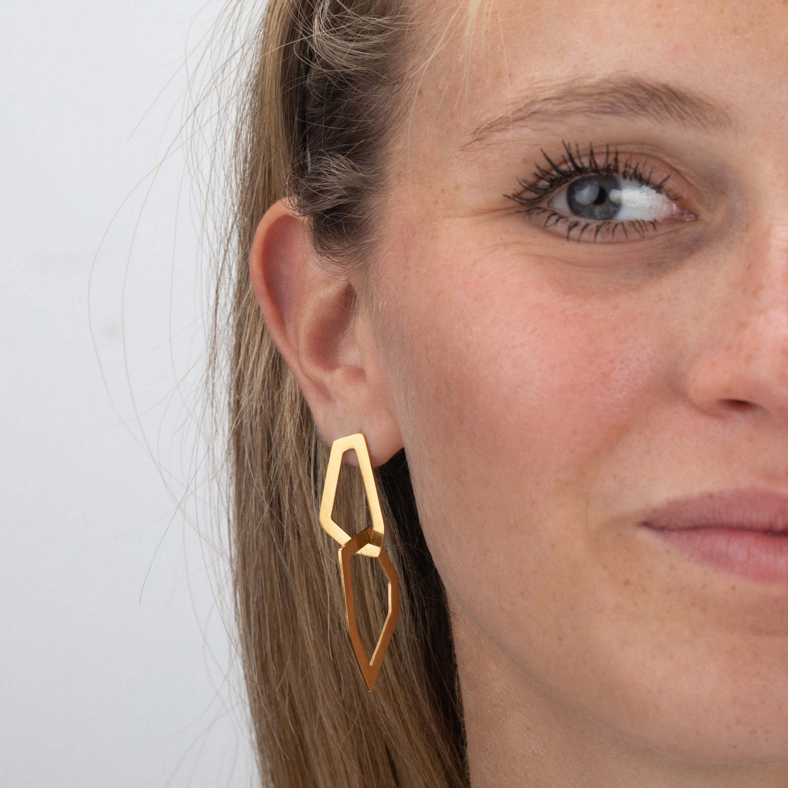 Brinco pendente dourado em mulher com cabelo louro