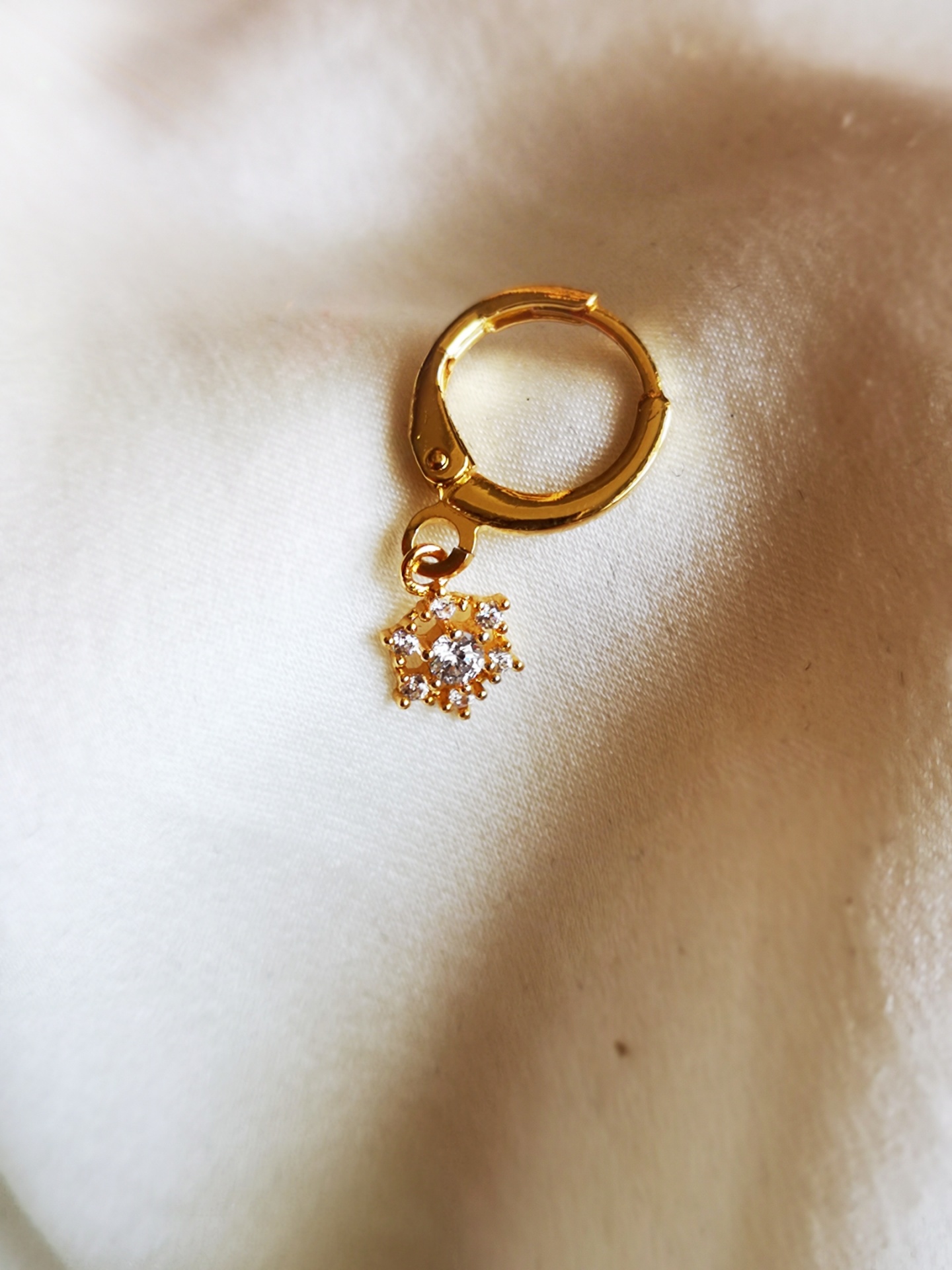 Brinco dourado com pendente em forma de estrela sobre tecido branco