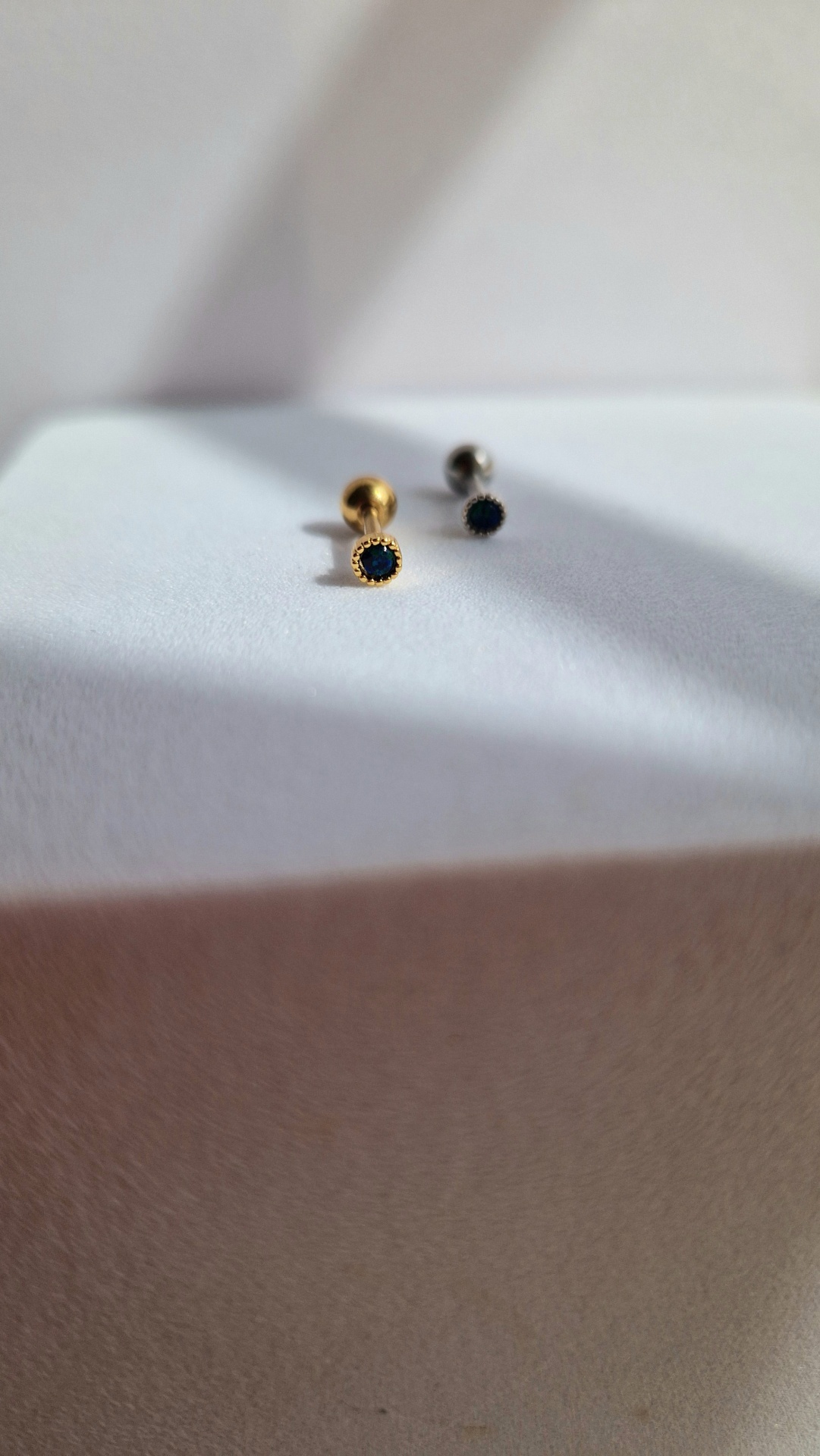 Dois brincos pequenos, dourado e prateado, com pedra preta circular