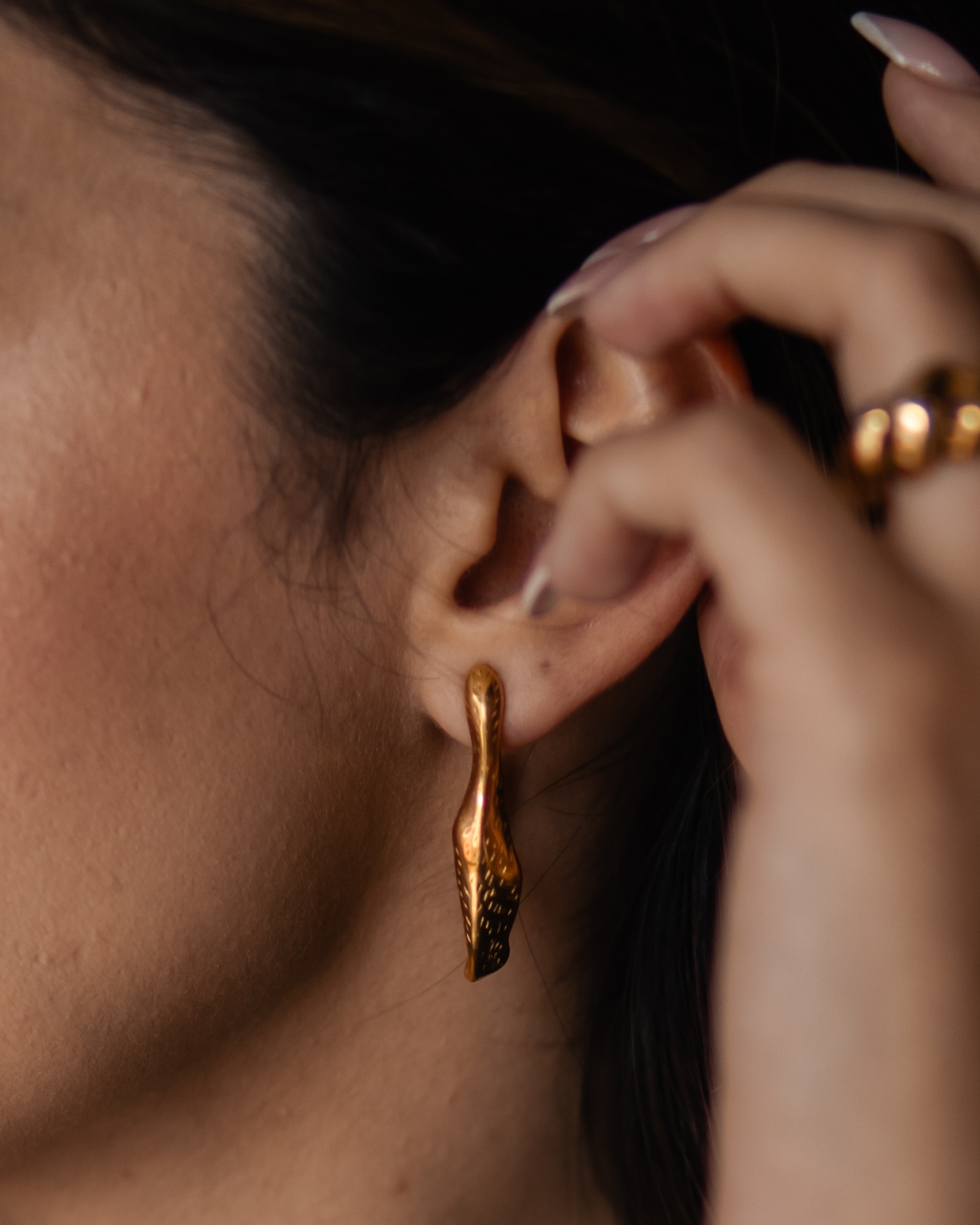 Brinco dourado em orelha de mulher com textura irregular