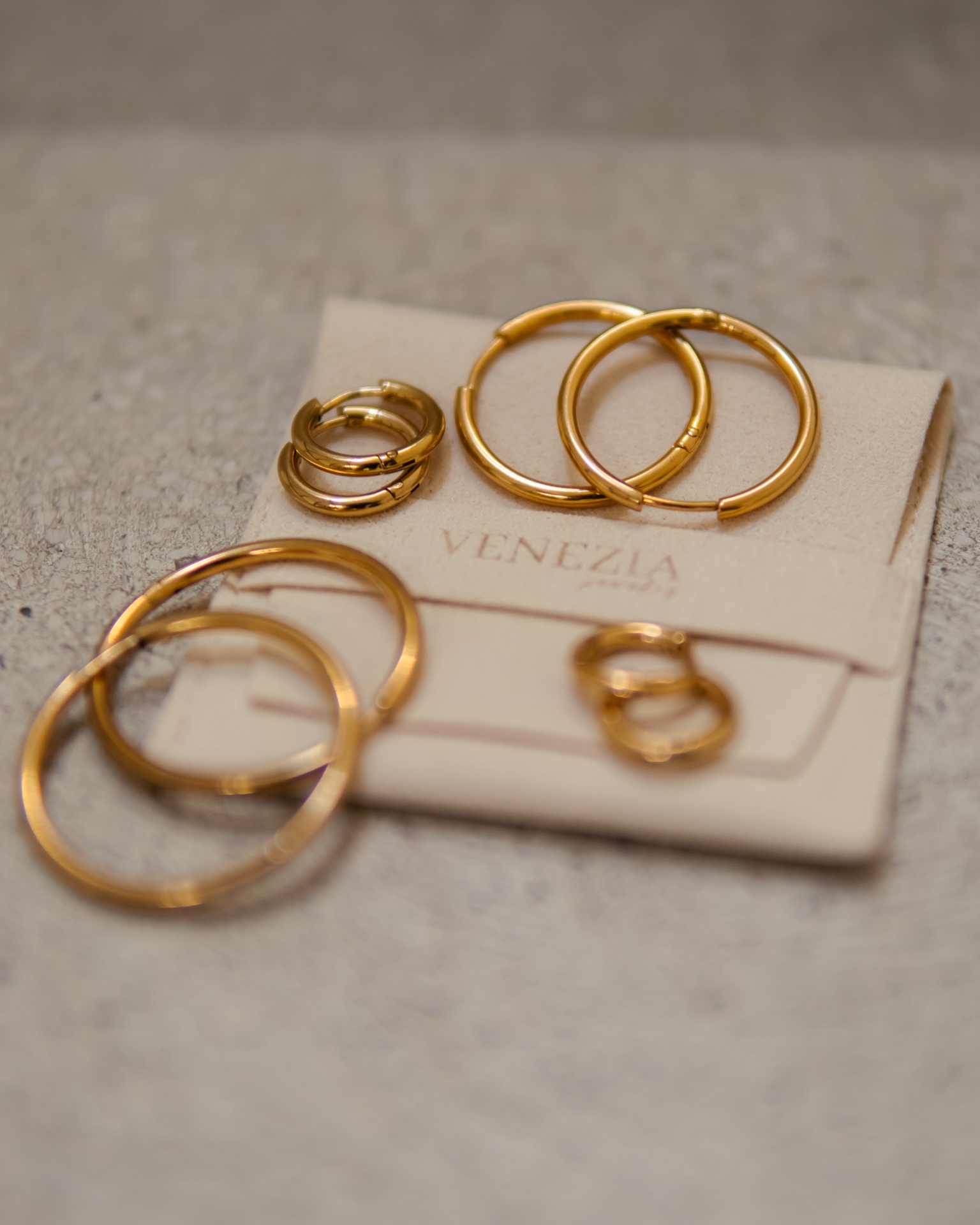 Brincos dourados de vários tamanhos e estilos em suporte de cartão com texto VENEZIA