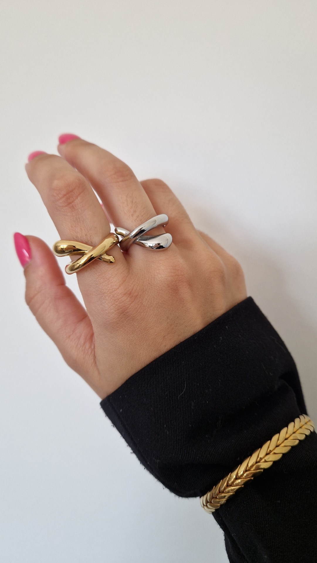 Anéis dourado e prateado em mão com unhas rosa e pulseira dourada