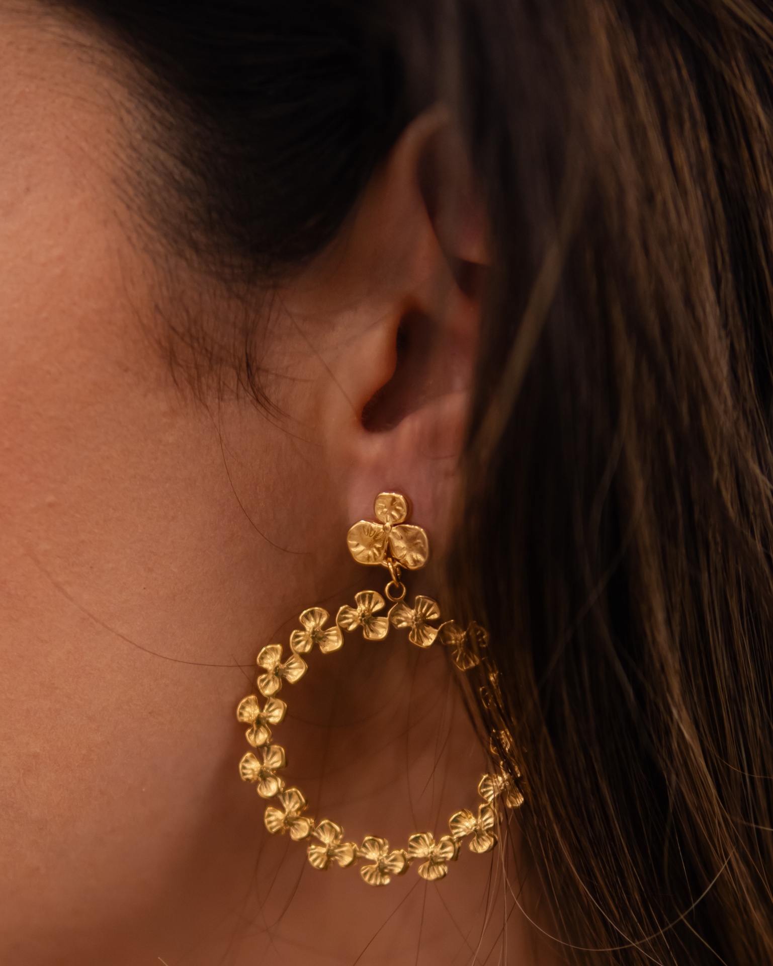 Brinco dourado em forma circular com flores, usado na orelha