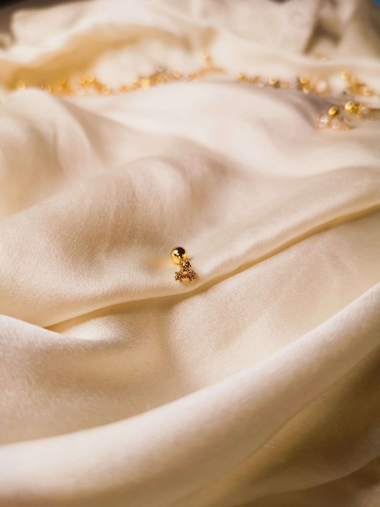 Tecido bege claro com pequenas peças douradas, incluindo uma bola dourada com pendente