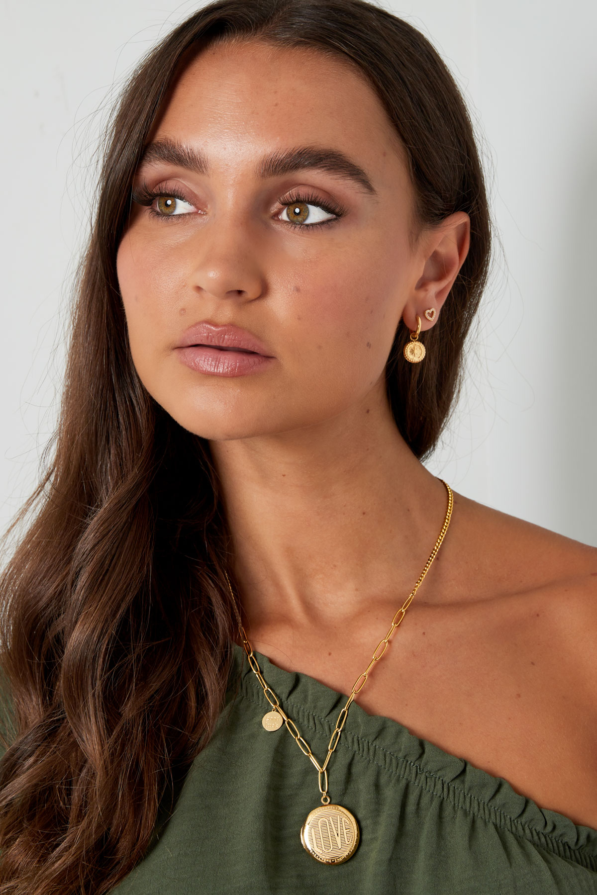 Mulher usando colar dourado com pendente LOVE e brincos dourados com pendentes redondos