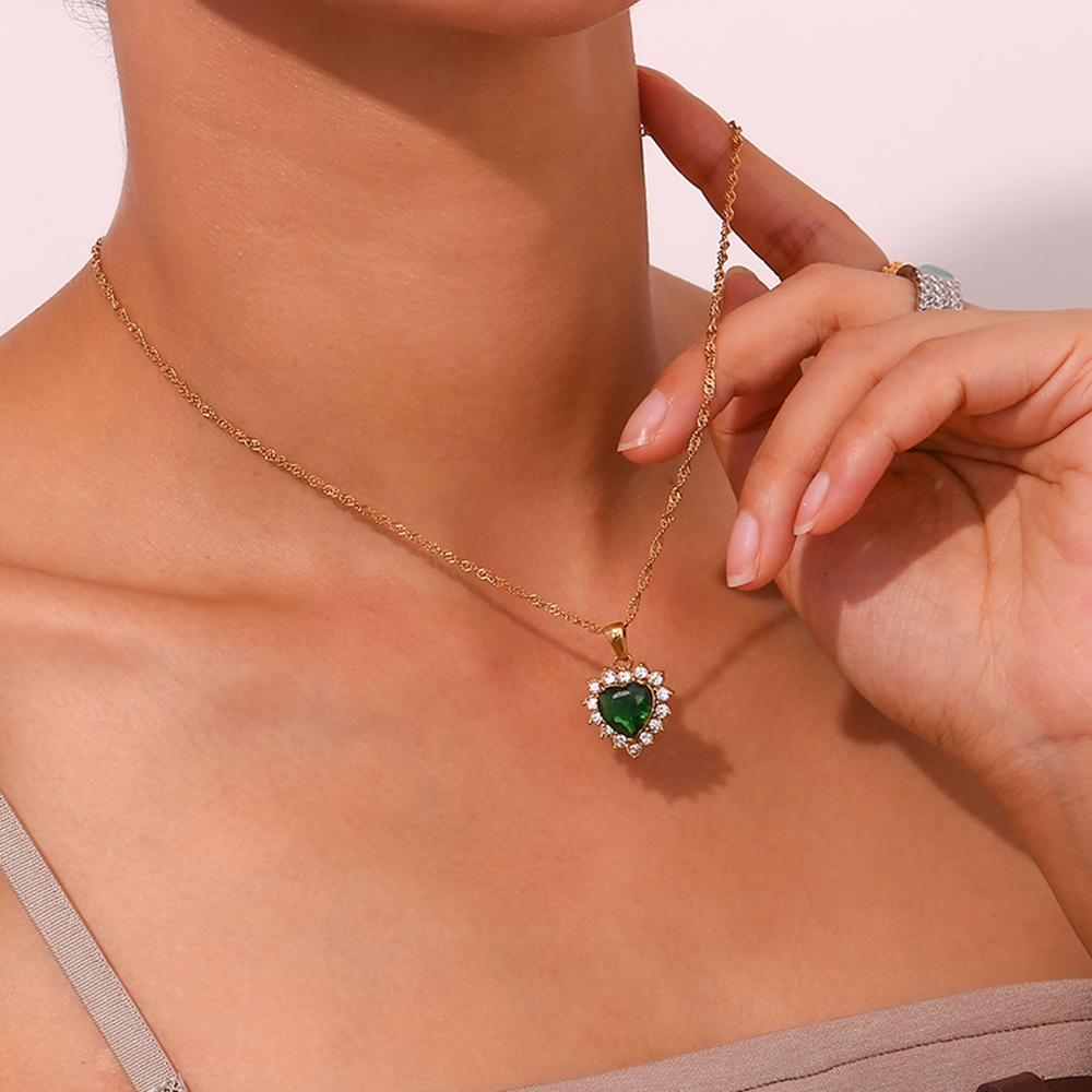 Colar dourado com pendente de coração verde e cristais claros no pescoço