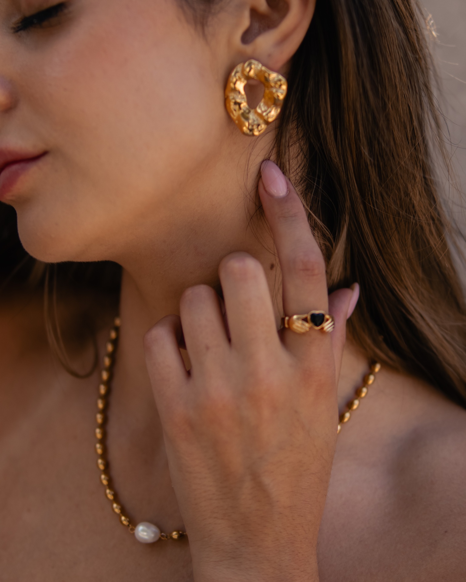 Brincos, anel e colar dourados com pérola branca usados por mulher