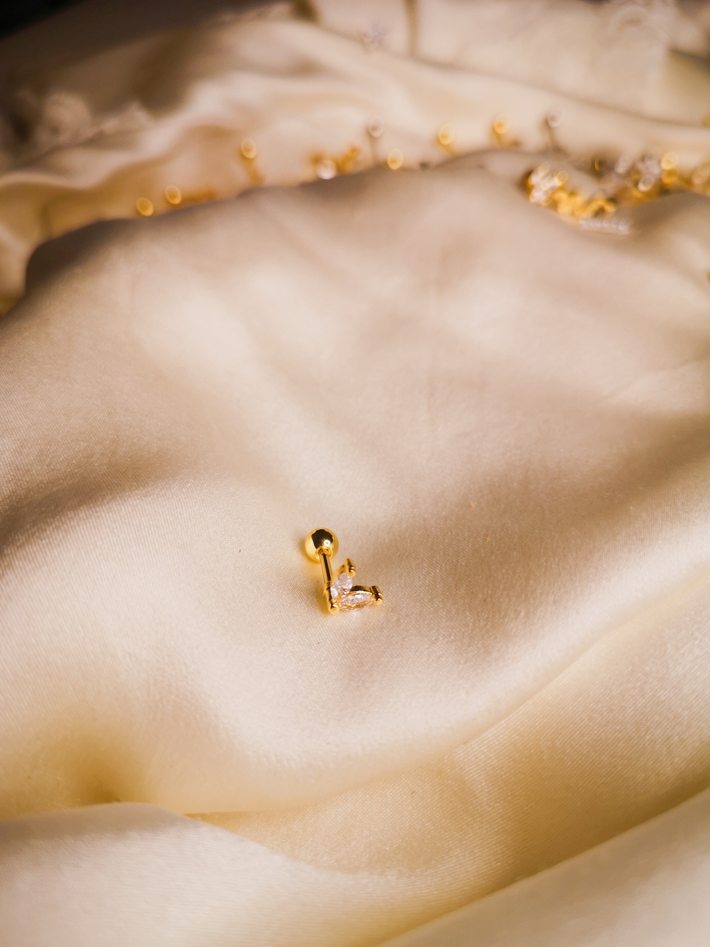 brinco dourado com pedra sobre tecido bege claro acetinado