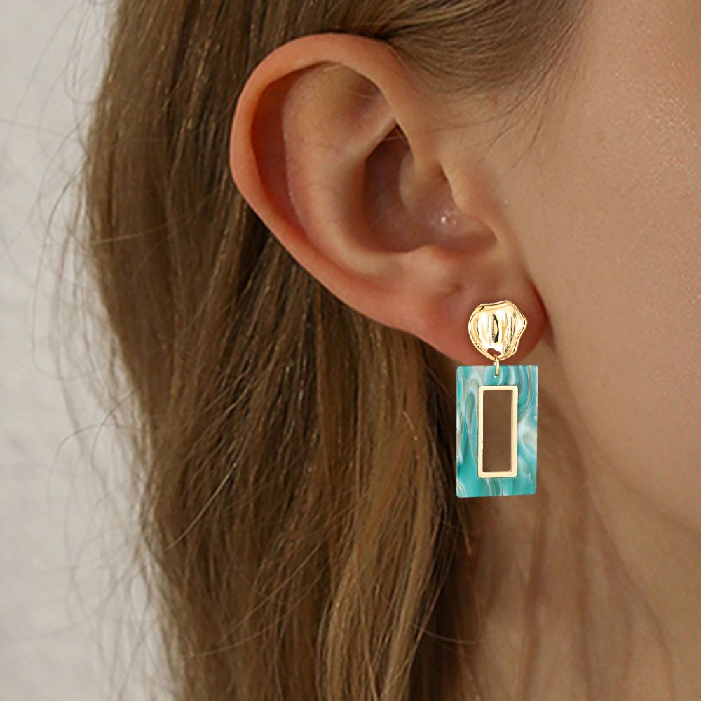 Brinco pendente dourado e azul turquesa usado na orelha