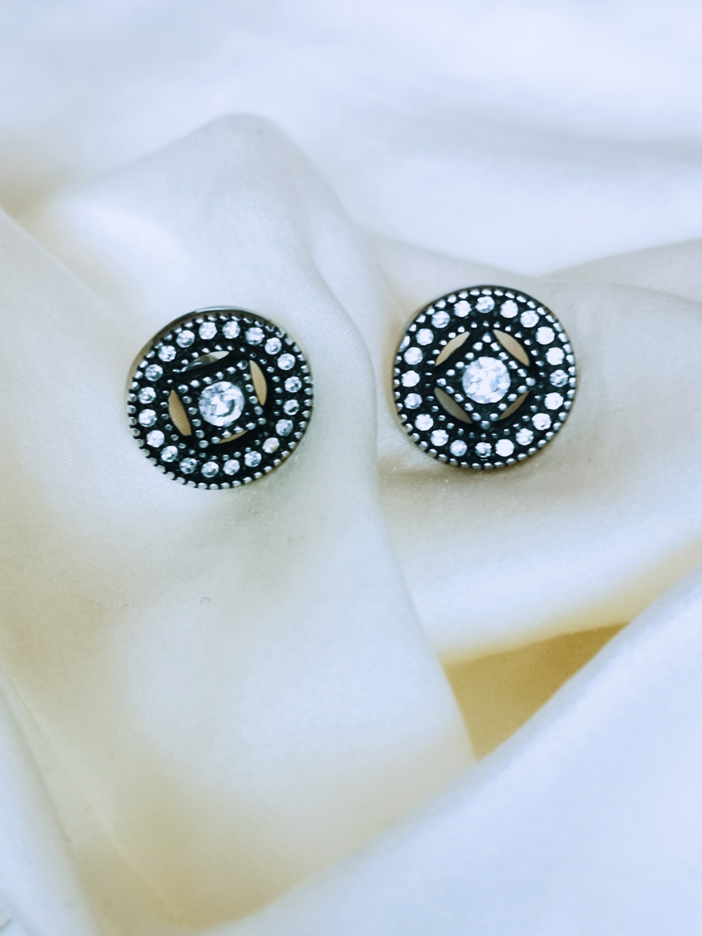 Brincos circulares em preto e branco com cristais sobre tecido branco