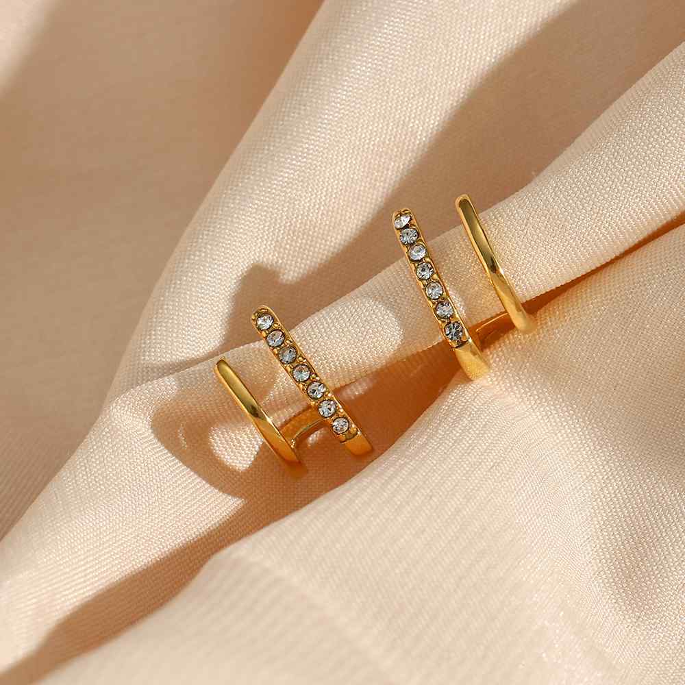 Brincos de argola dourados com pedras cristalinas sobre tecido creme