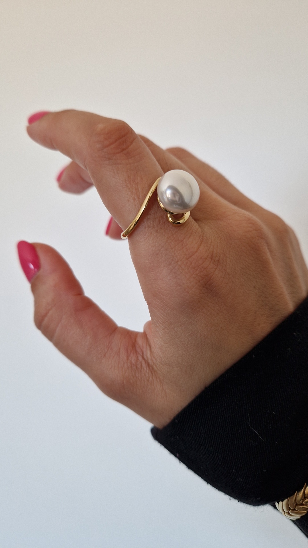 Anel dourado com pérola branca numa mão com unhas rosas