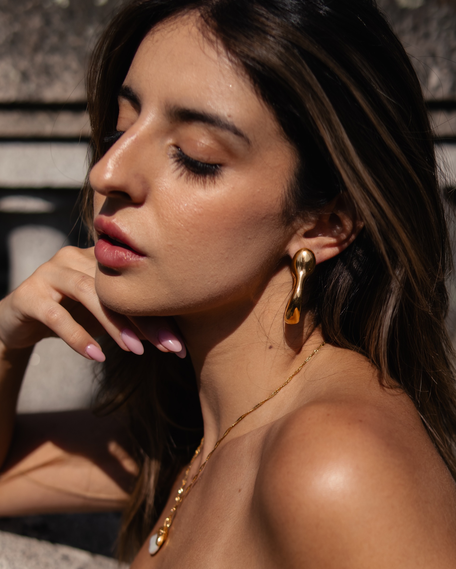 Mulher com brincos dourados pendentes e colar dourado com pendente redondo