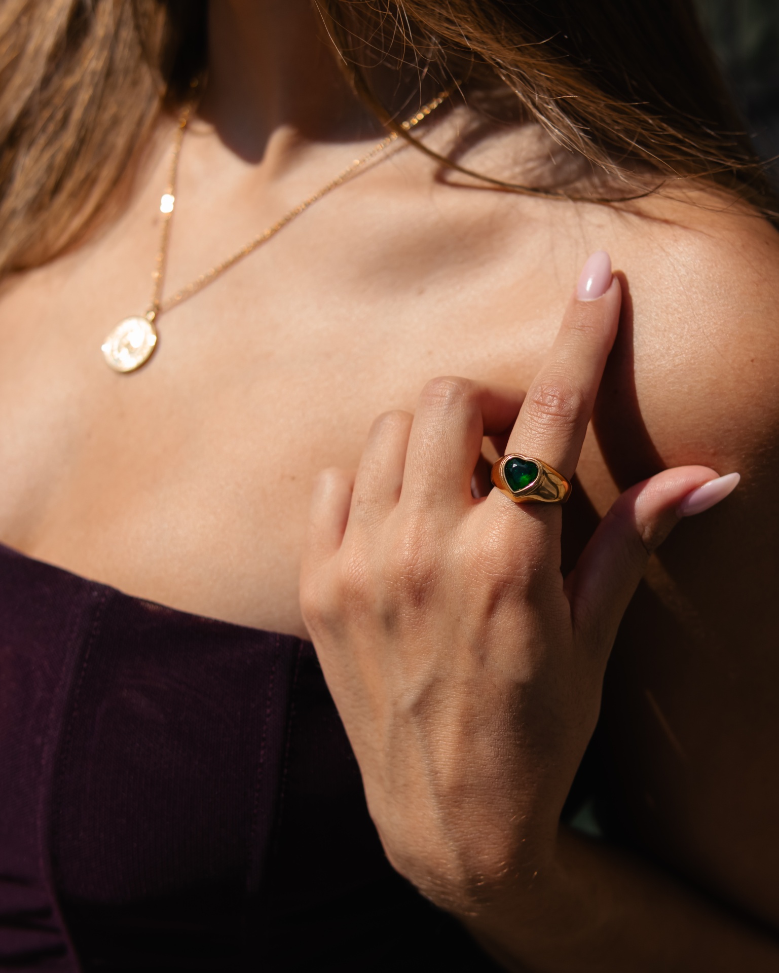 anel dourado com pedra verde em forma de coração na mão de mulher com vestido roxo escuro