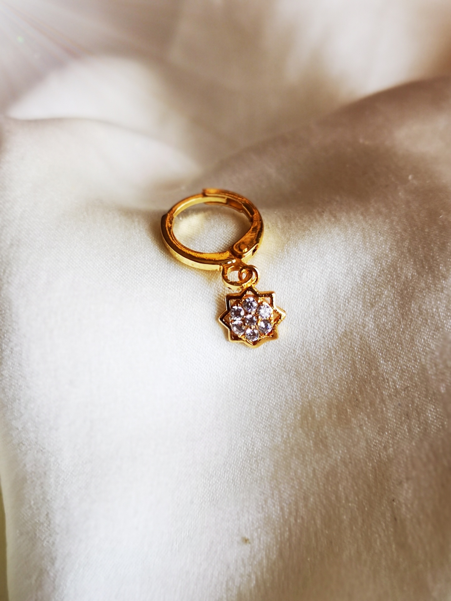 Brinco dourado com pendente de flor e pedras sobre tecido branco