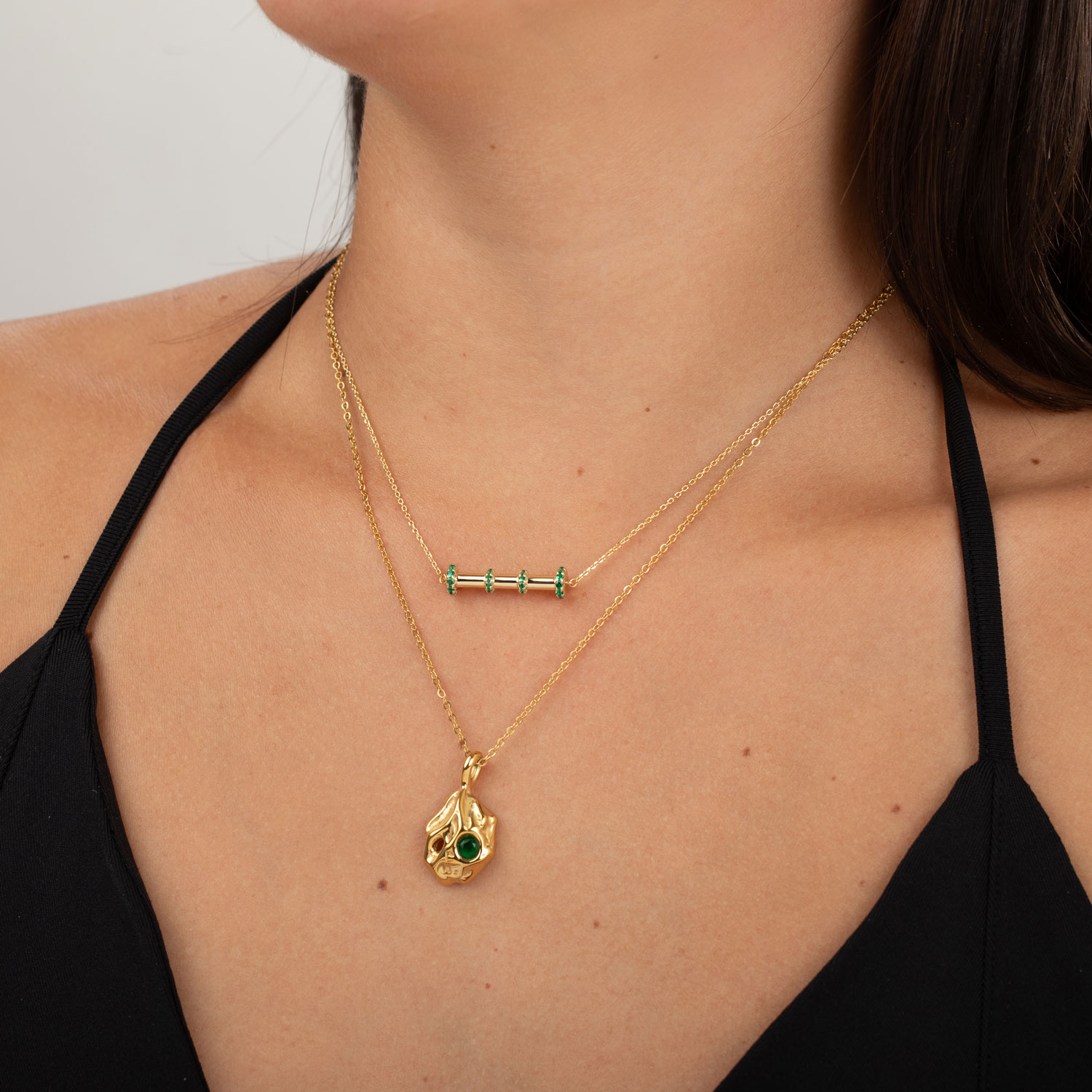 Colares dourados com pedras verdes usados por mulher com top preto