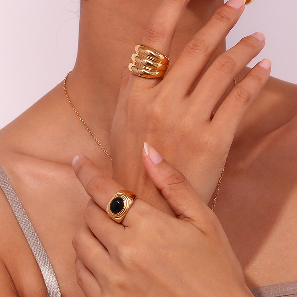Mãos com dois anéis dourados, um com pedra preta, sobre fundo branco