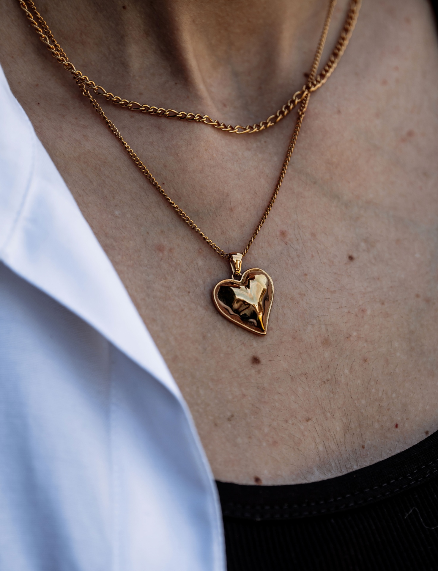 Colar dourado com pendente em formato de coração no pescoço de uma pessoa