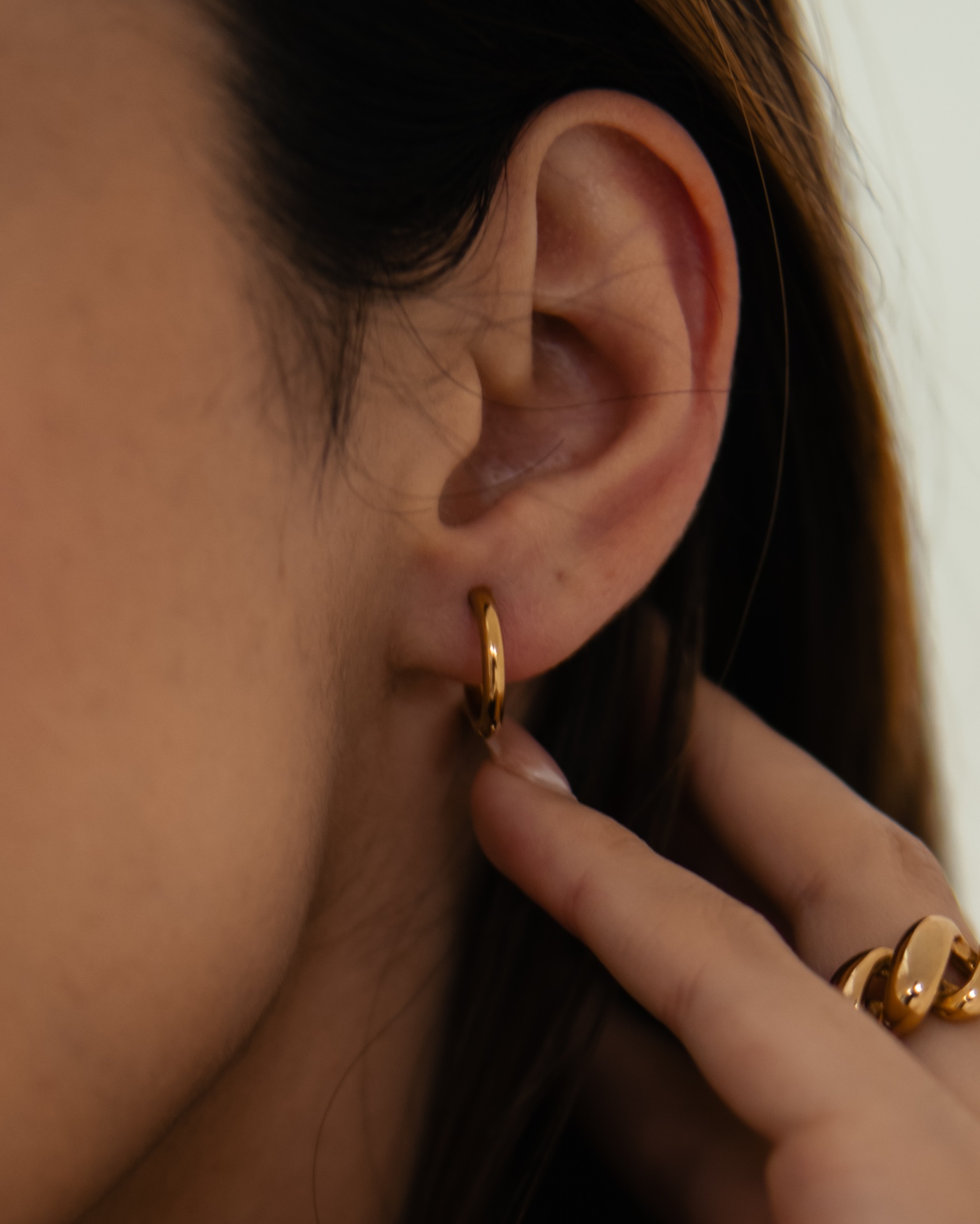 Orelha com brinco de argola dourado e mão com anel dourado