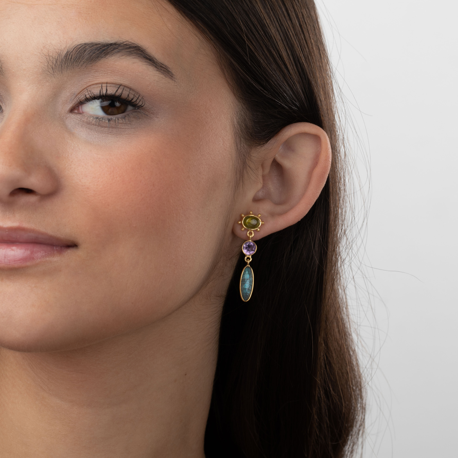 Brincos dourados com pedras coloridas usados por mulher