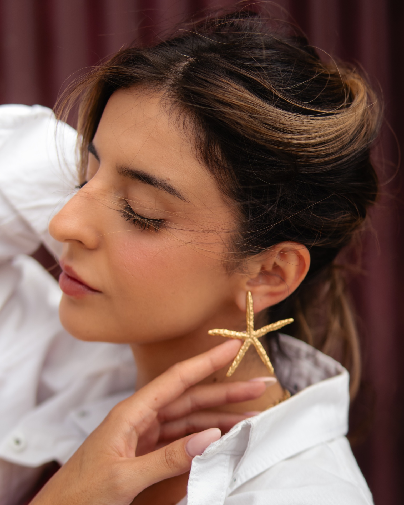 Brincos de estrela do mar dourados em mulher com camisa branca