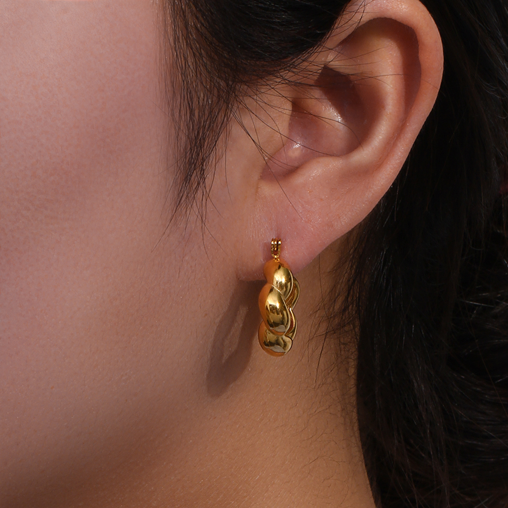 Brinco dourado ondulado na orelha de uma pessoa