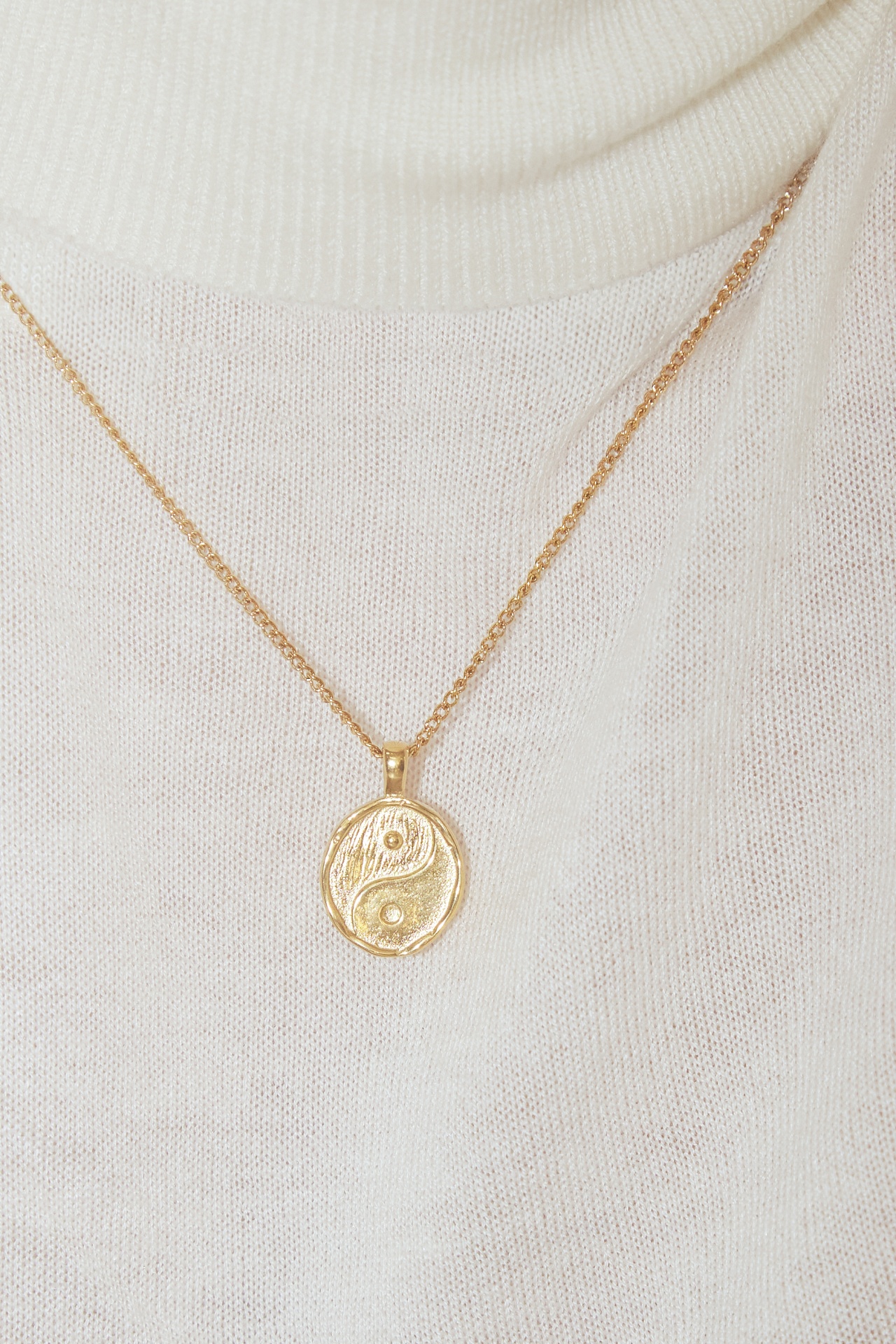 Colar dourado com pendente yin-yang sobre camisola branca de malha