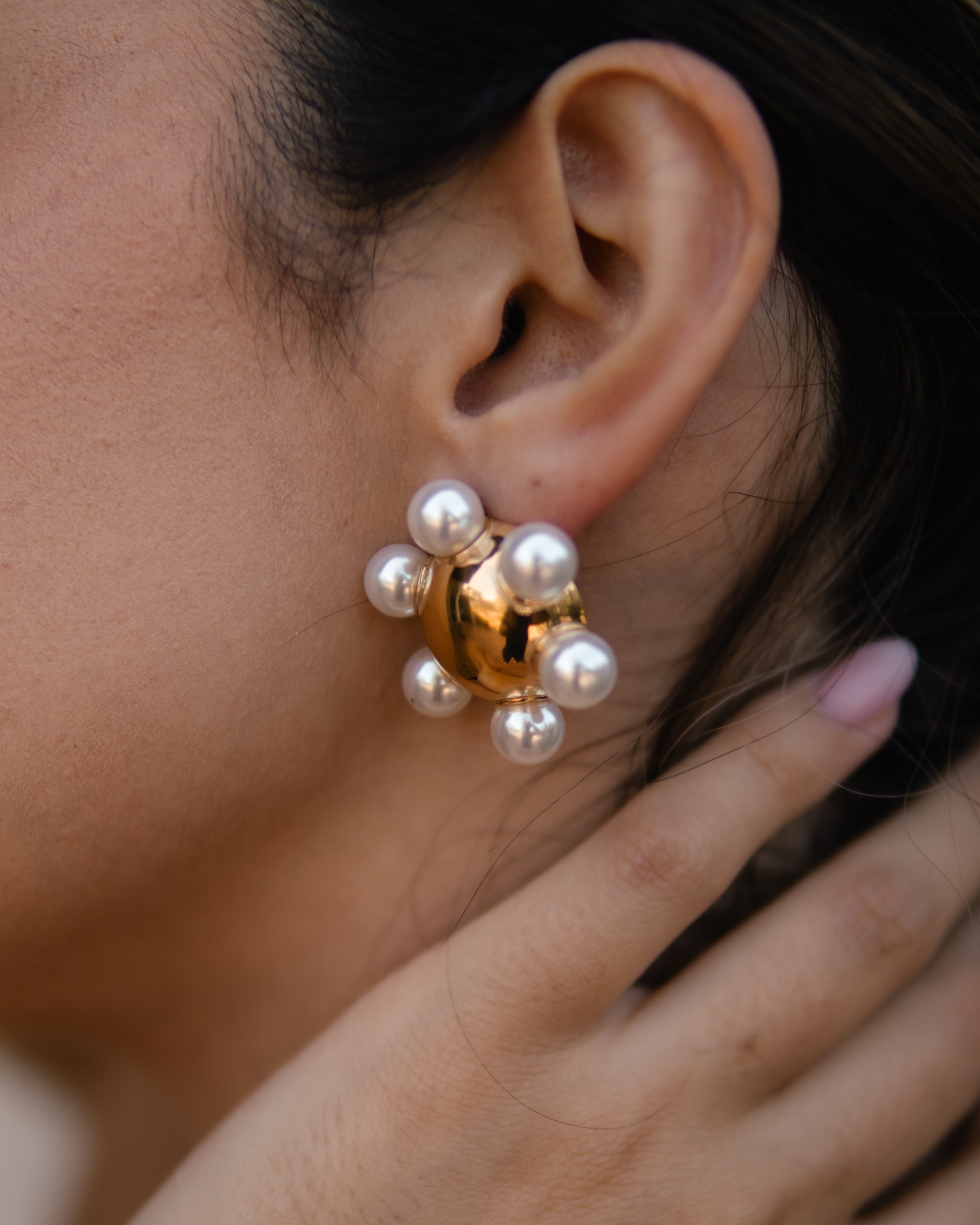Brinco dourado esférico com pérolas brancas em orelha de pessoa