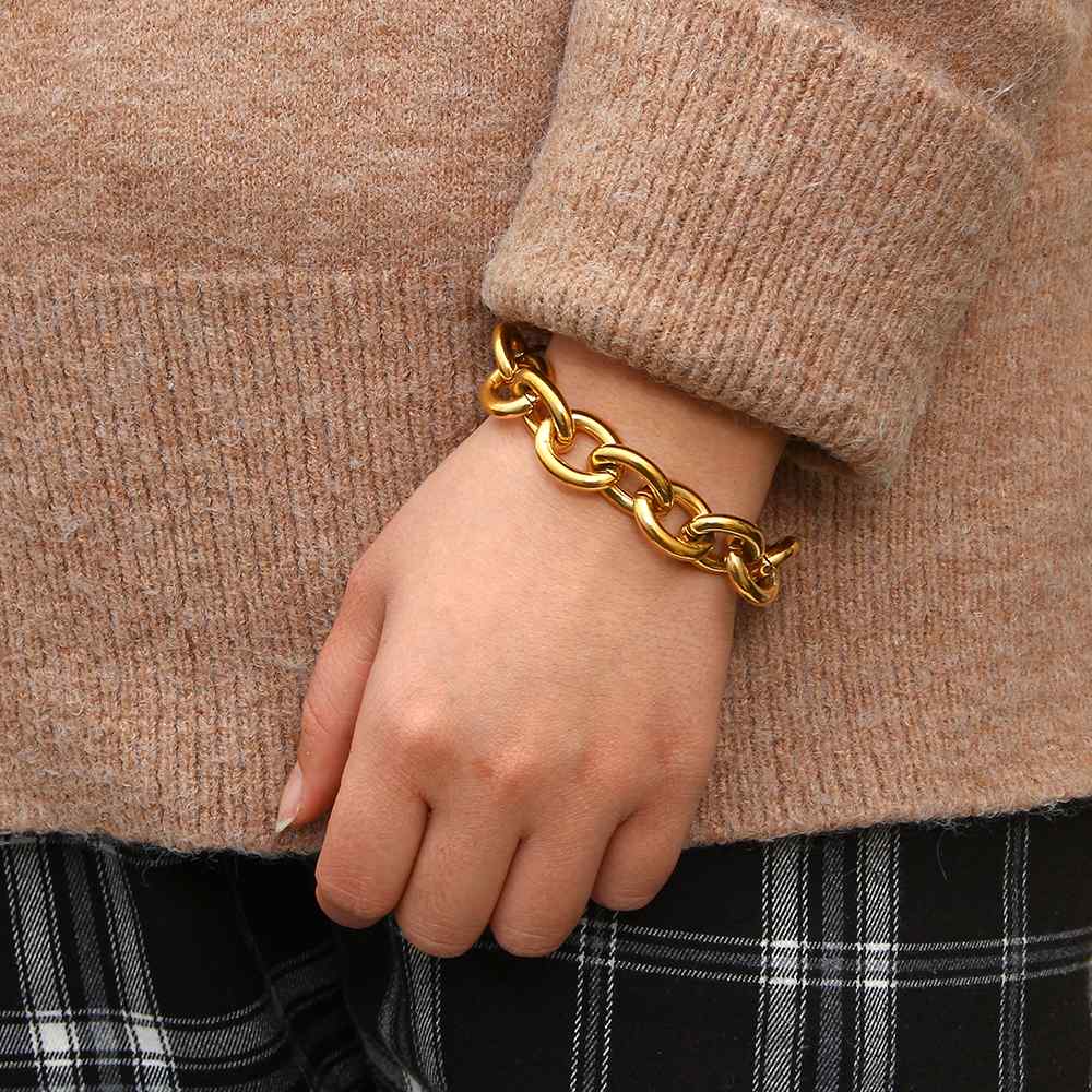 Pulseira dourada grossa em pulso feminino com camisola castanha e calças xadrez