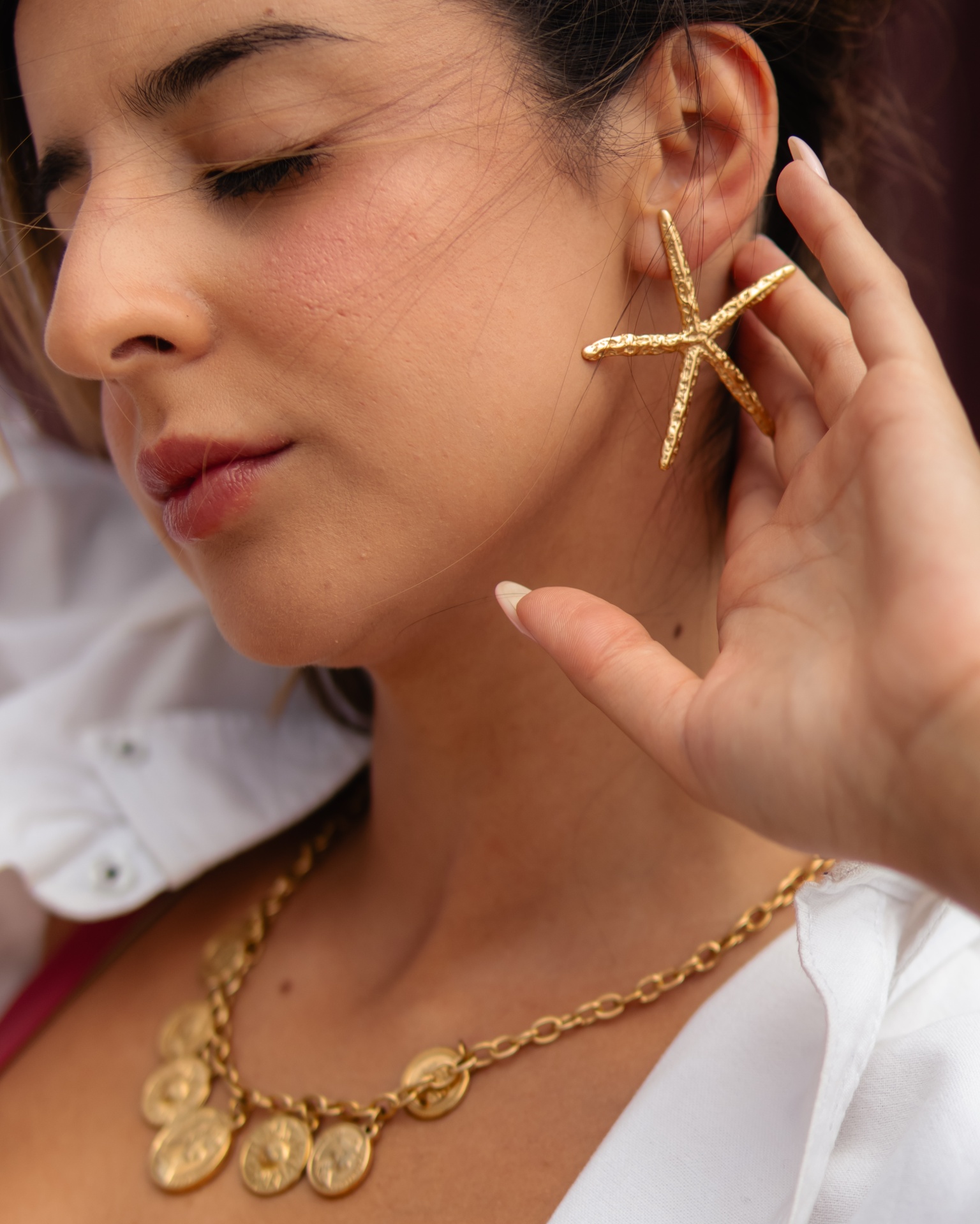 Brincos dourados estrela do mar e colar com moedas em mulher