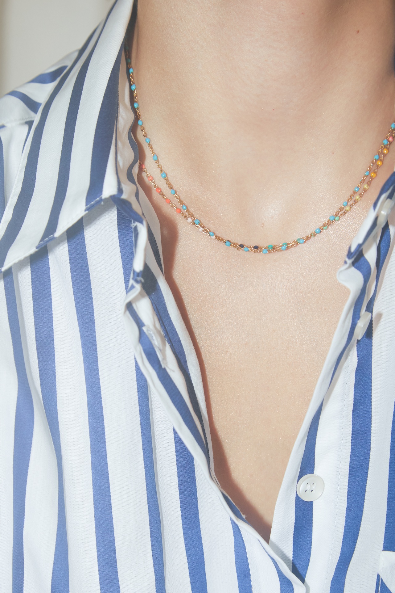 Colar delicado duplo com pedras coloridas usado com camisa branca às riscas azuis