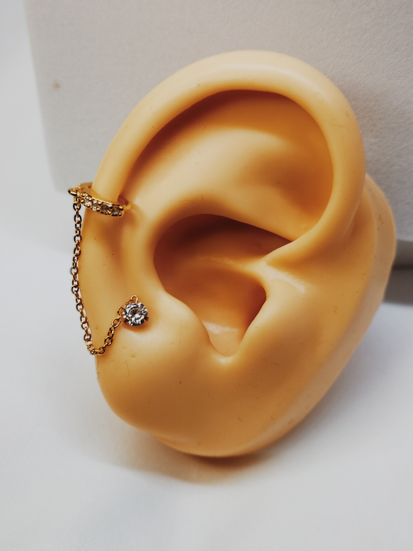 Brincos dourados com corrente e pedra brilhante em orelha artificial bege